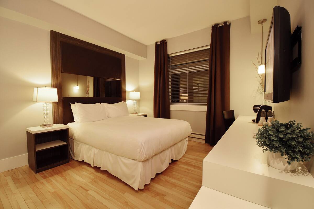 A neatly arranged bedroom with a bed, bedside tables, a dresser, a mirror, and a window with curtains.