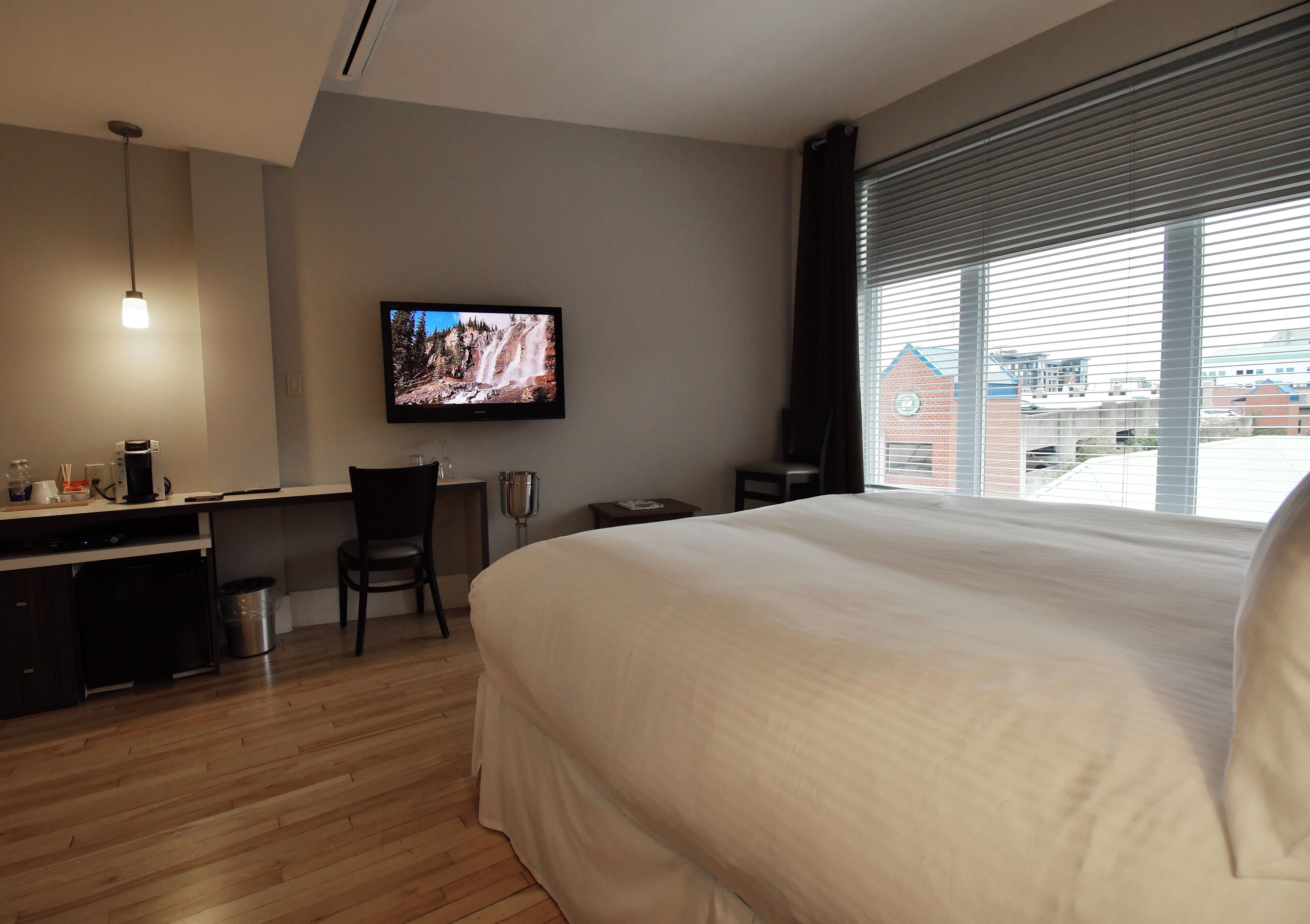 Habitación de hotel con una cama grande, un escritorio con silla, un televisor y una ventana con persianas.