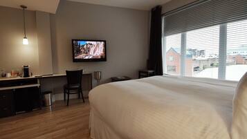 Habitación de hotel con una cama grande, un escritorio con silla, un televisor y una ventana con persianas.