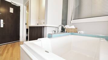 Un baño moderno con una bañera grande, un espejo y una ventana con persianas.