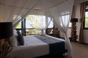 A bed with white linens, a blue and white patterned bedspread, and a canopy. There is a chair and a small table in the background.