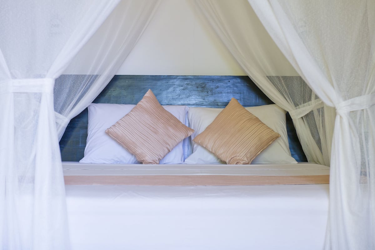 Una cama con cabecera de madera, ropa de cama blanca y dos almohadas color beige.