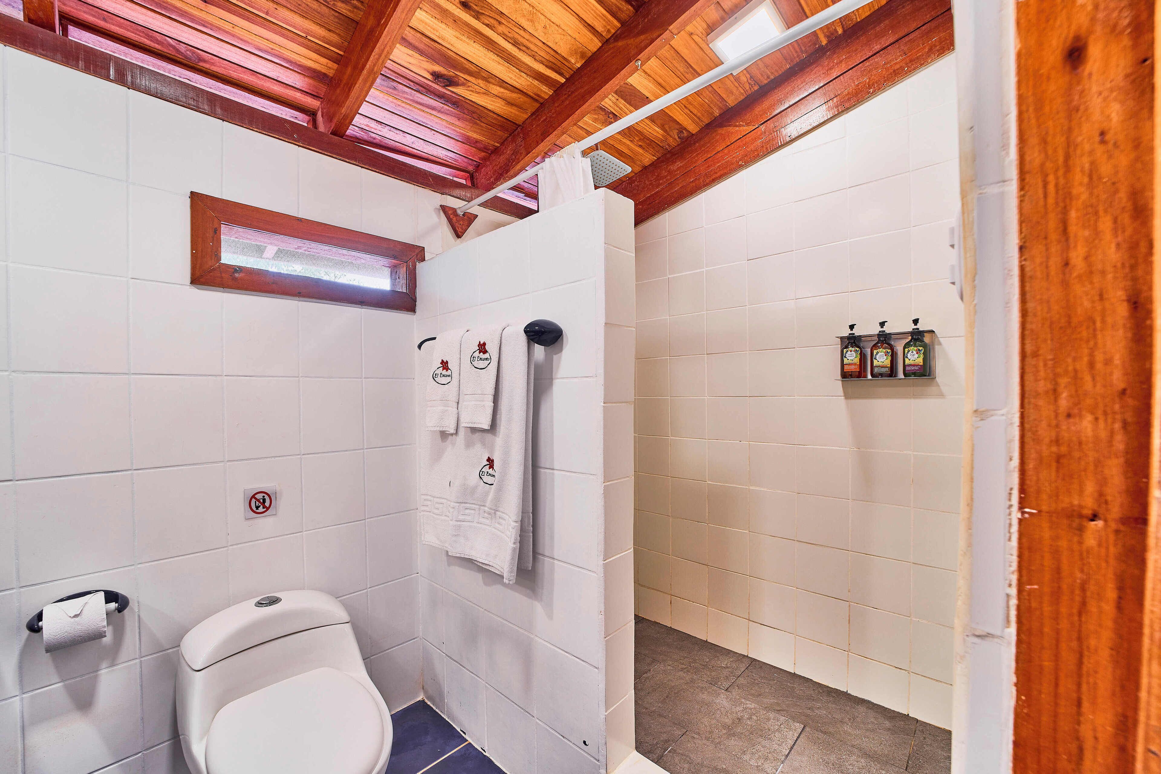 A bathroom with a toilet, a shower, and a towel rack with towels.