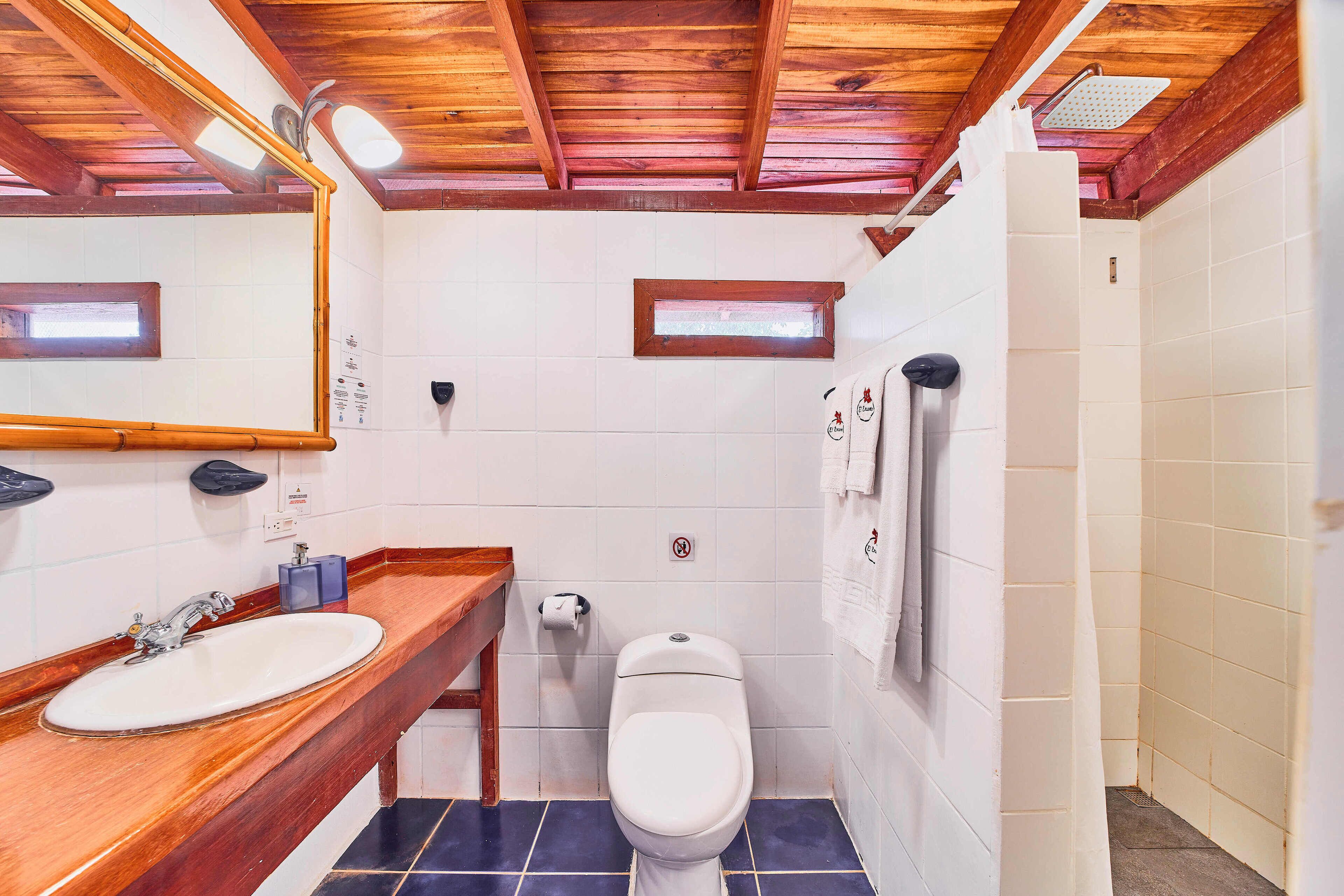 Een badkamer met een houten wastafelmeubel, een witte wasbak, toilet en douche.