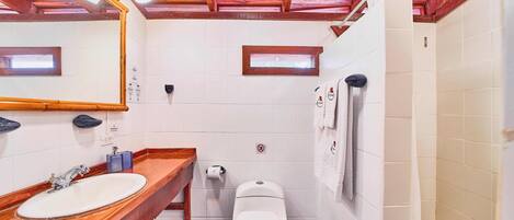 A bathroom with a wooden vanity, a white sink, a toilet, and a shower area.