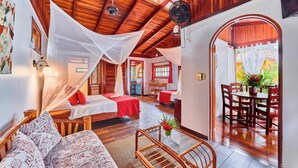 A room with a bed, a sofa, a dining table with chairs, and a fan. - Hotel El Encanto (Cahuita)