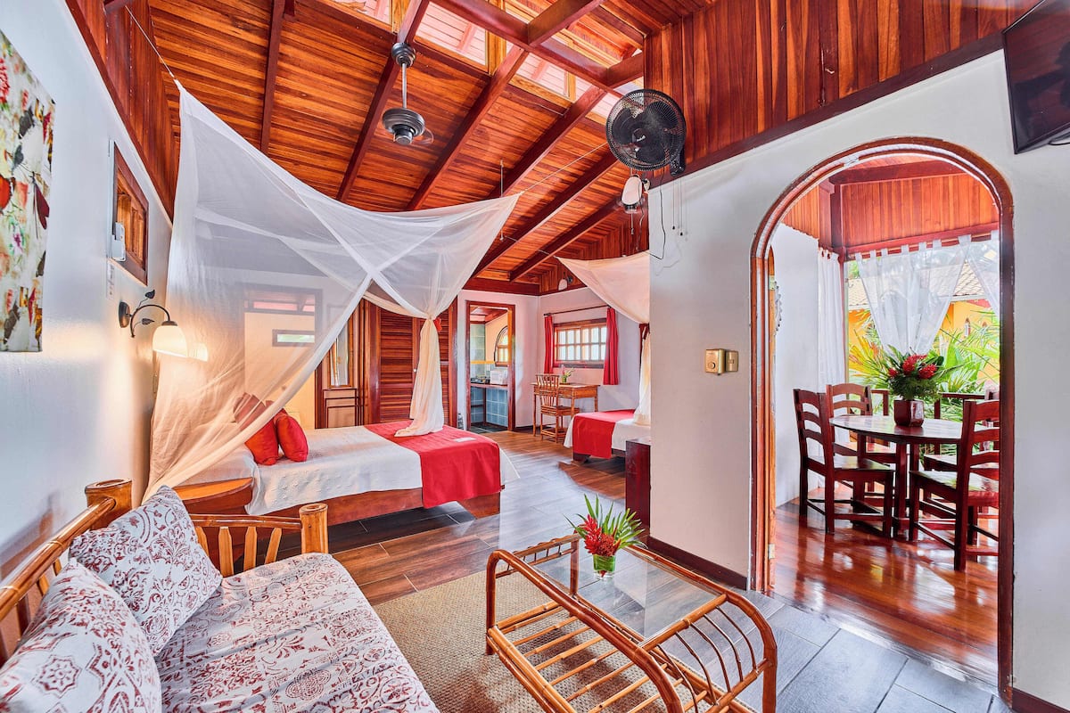 A room with a bed, a sofa, a dining table with chairs, and a fan.