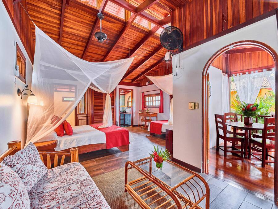 A room with a bed, a sofa, a dining table with chairs, and a fan.