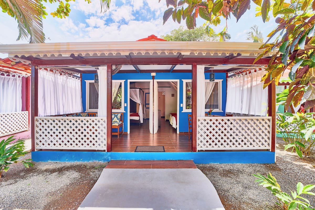 A covered outdoor area with a wooden floor, white lattice panels, and a blue and red building in the background.
