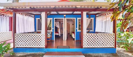 A covered outdoor area with a wooden floor, white lattice panels, and a blue and red building in the background.