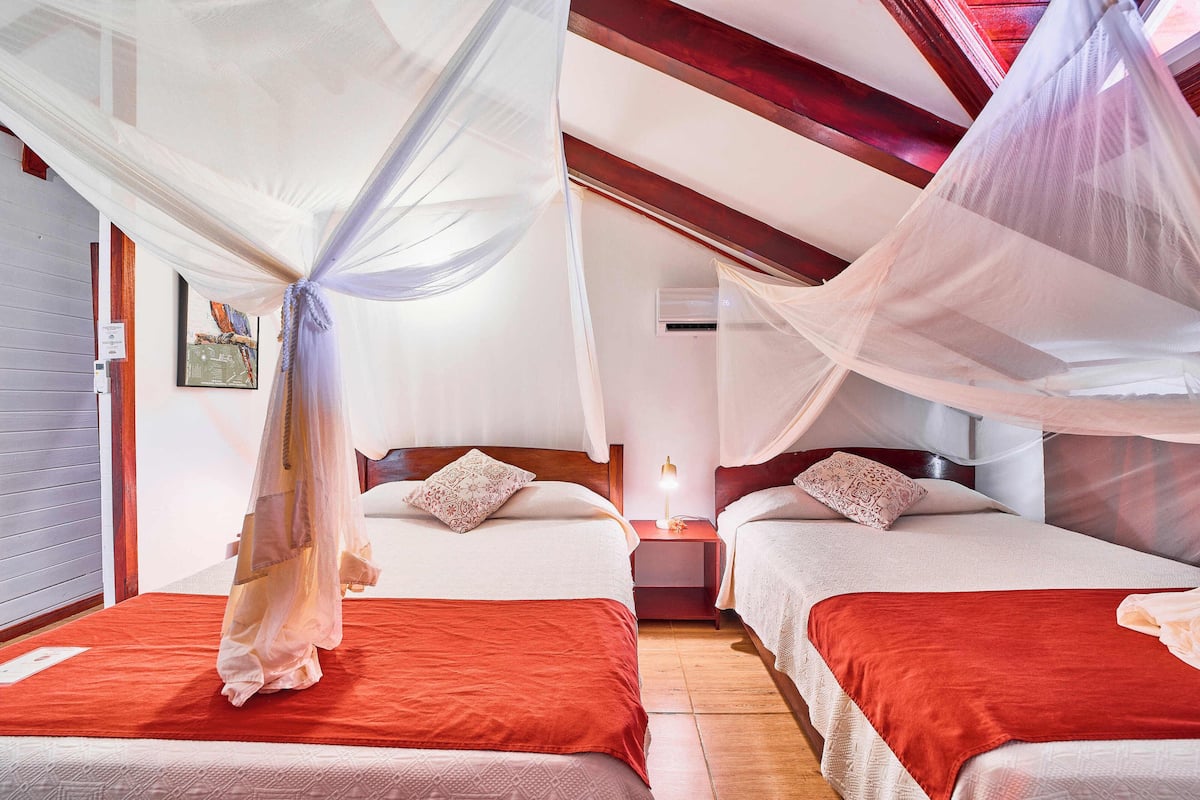 A room with two beds, each with a red bedspread and white pillows, and a canopy bed with a sheer white canopy.