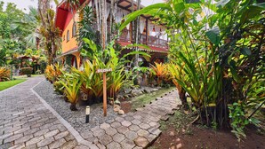 A tropical garden with a pathway leading to a building with a red roof and balconies. - Hotel El Encanto (Cahuita)