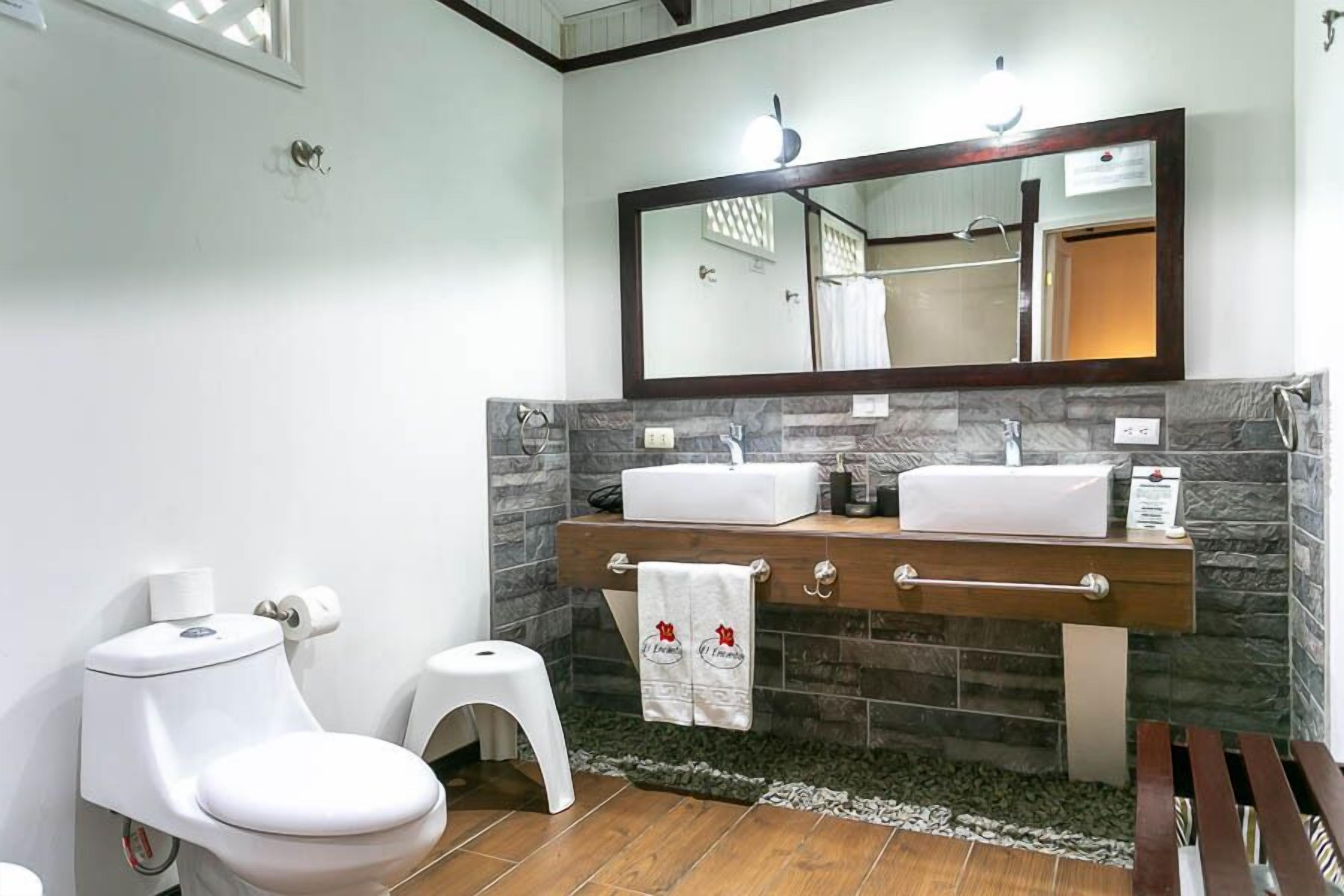 A bathroom with a white toilet, a sink with a mirror above, and a small stool.
