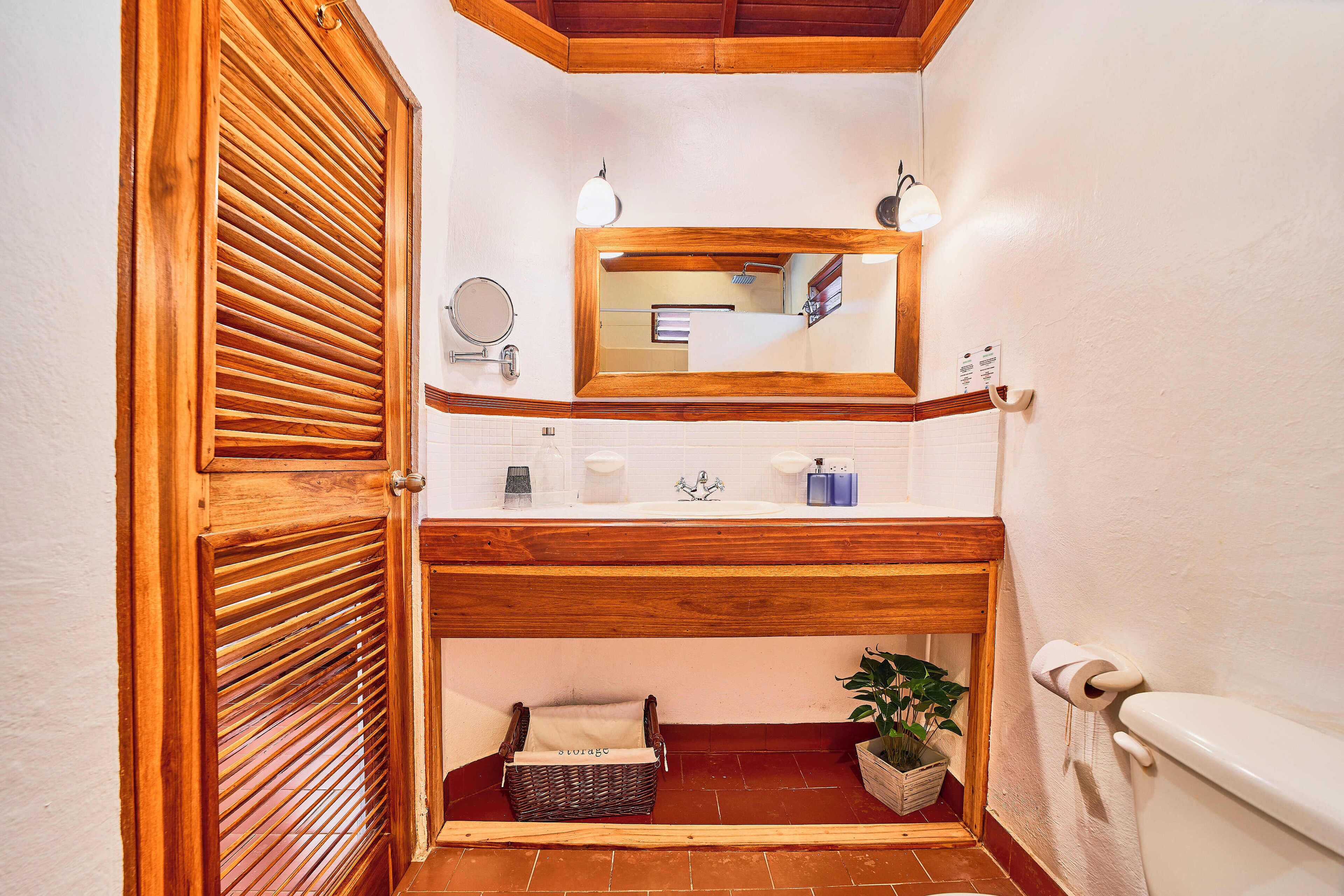 A bathroom with a wooden vanity, a mirror, a sink, a toilet, and a small storage basket.