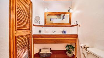 A bathroom with a wooden vanity, a mirror, a sink, a toilet, and a small storage basket.