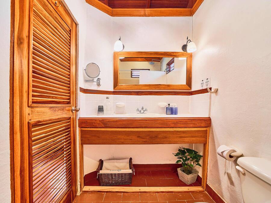 A bathroom with a wooden vanity, a mirror, a sink, a toilet, and a small storage basket.