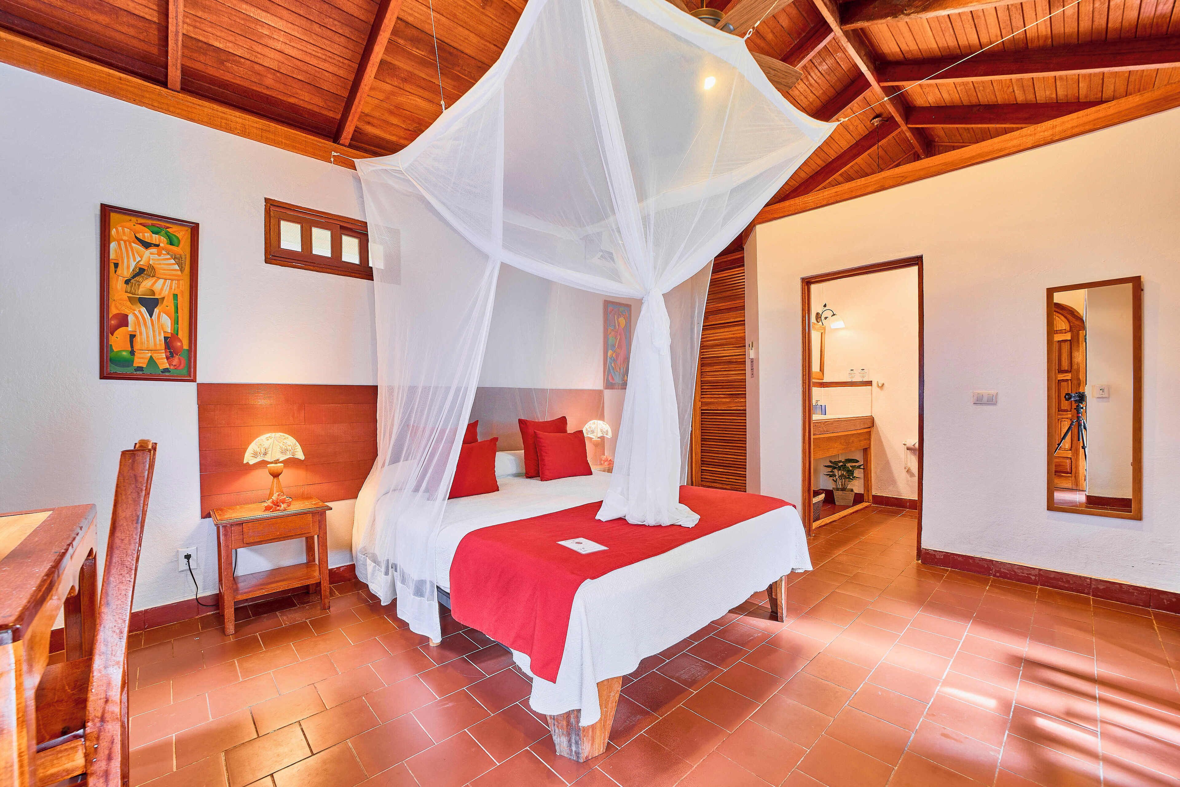 A bedroom with a four-poster bed, wooden headboard, and a red bedspread.