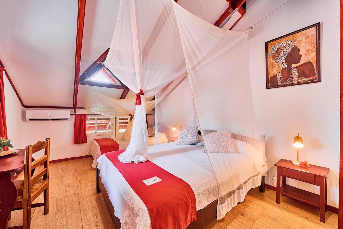 A bedroom with a bed under a canopy, a bedside table with a lamp, and a wall-mounted air conditioner.