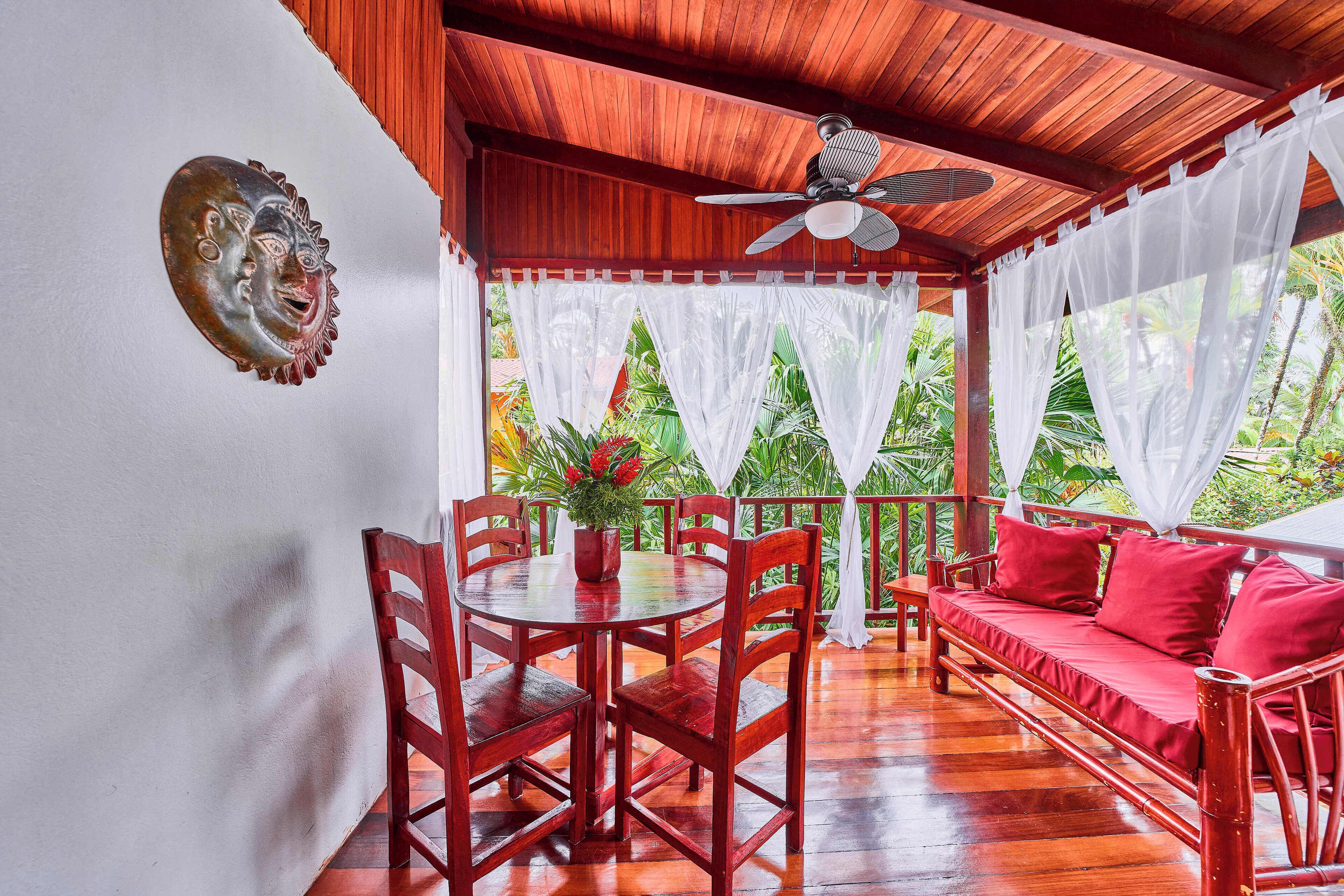 Una habitación con piso de madera, una mesa de comedor con sillas, un sofá rojo y un ventilador de techo.