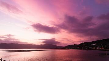 A sunset over a calm body of water with distant hills and a few buildings on the shore.