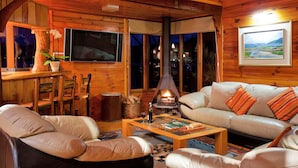 A cozy cabin interior with a fireplace, leather sofas, and a dining area.