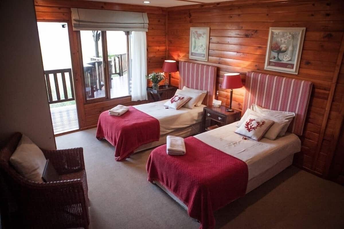 A wooden cabin-style room with two beds, a wicker chair, and a balcony.