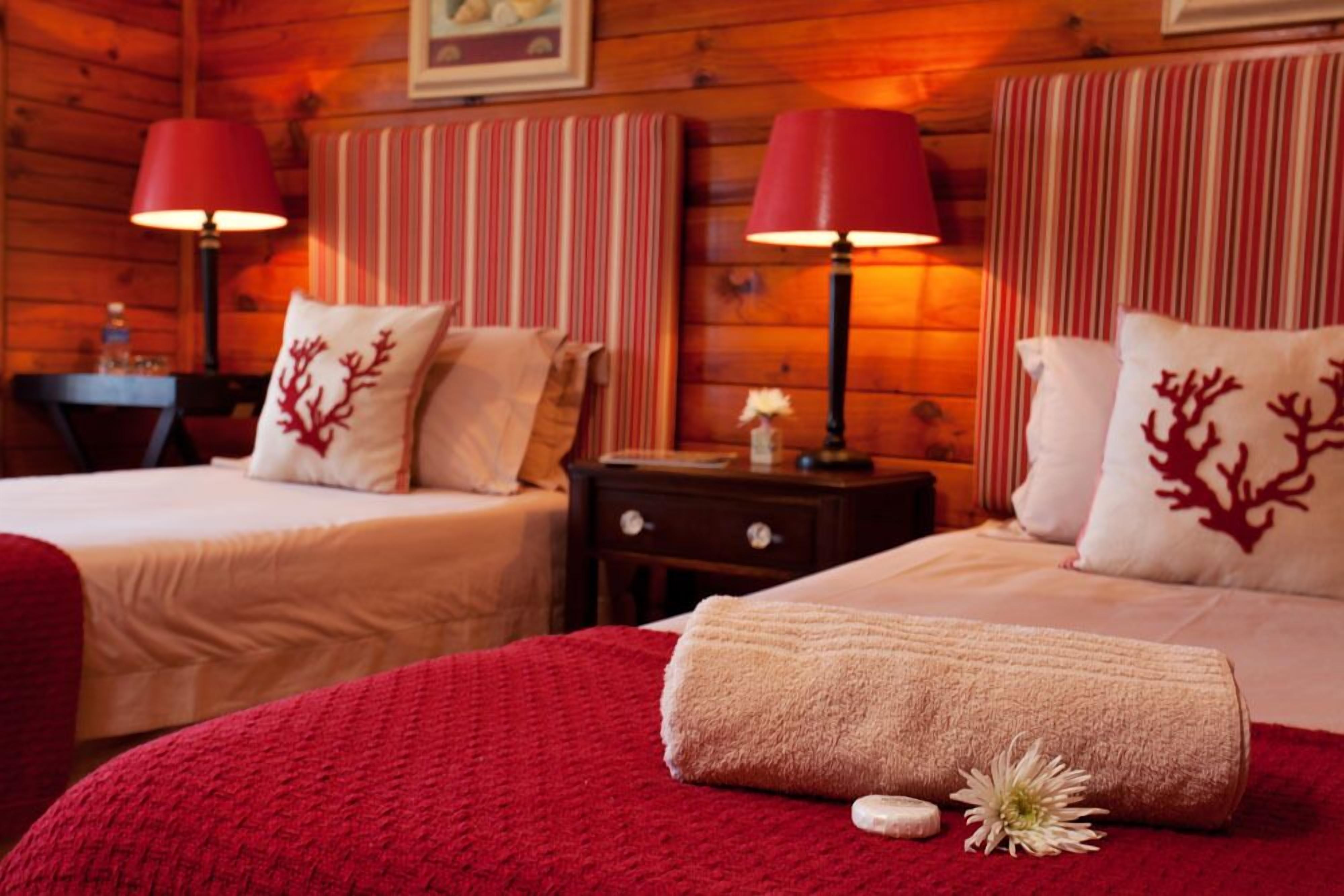 A cozy room with two beds, each with a red lamp and striped headboard.