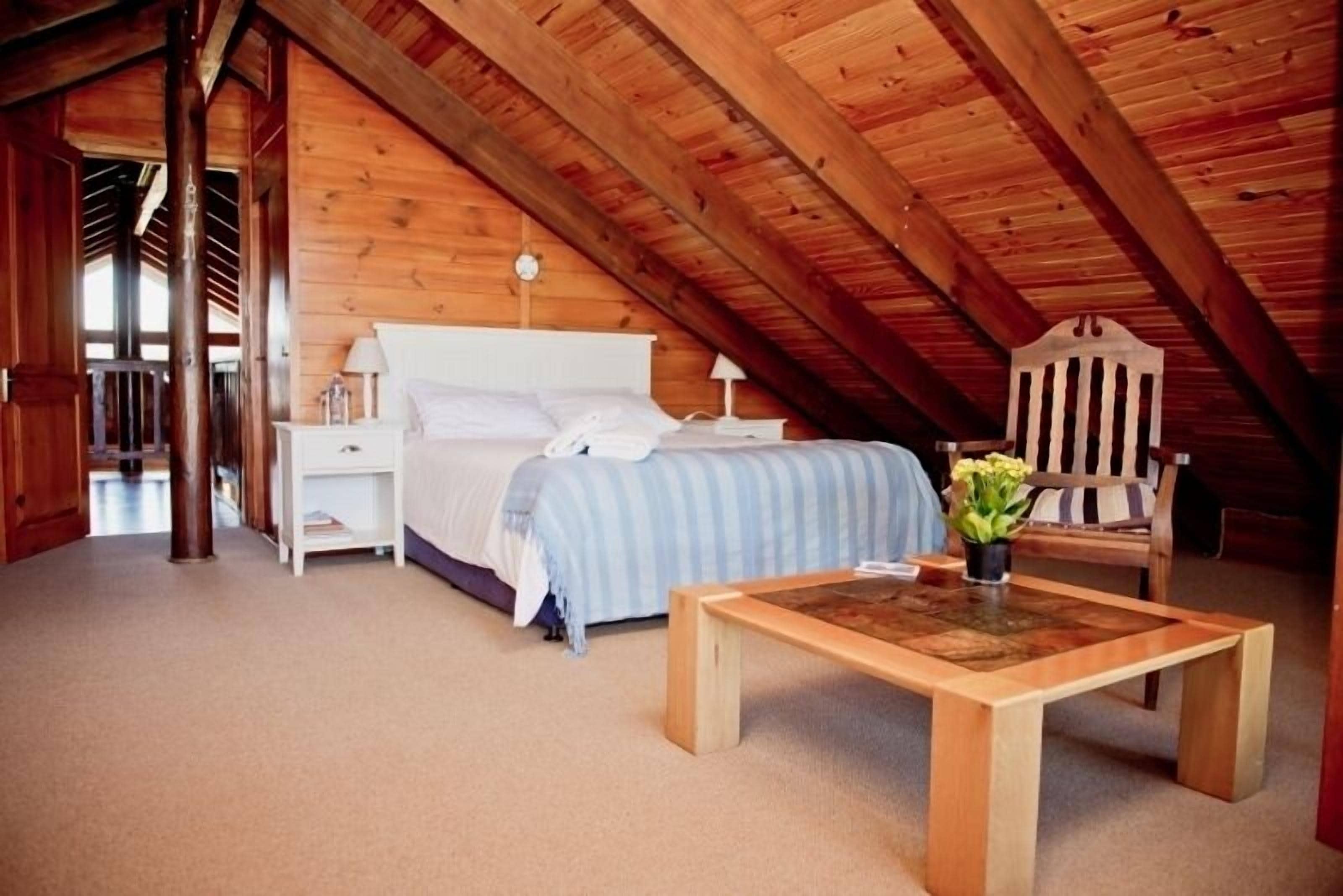 Une chambre avec un plafond en bois, un lit avec une tête de lit blanche, une table de chevet avec une lampe et une chaise avec un coussin.