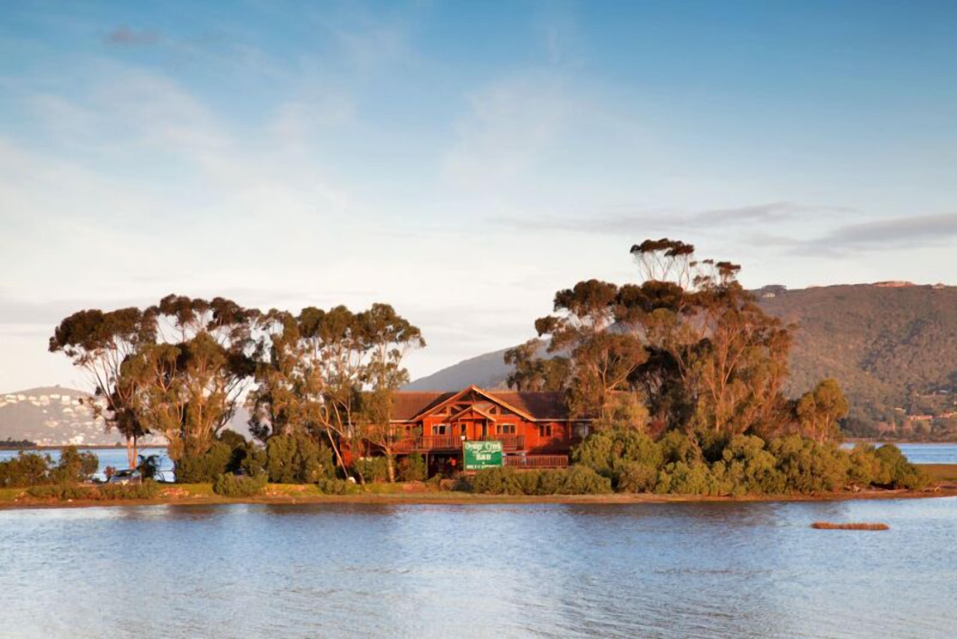 A large, red wooden house with a balcony, surrounded by trees and a lake.