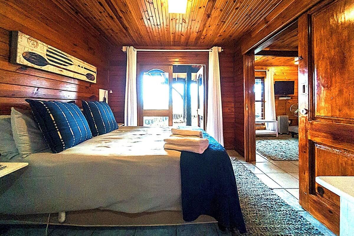A wooden cabin bedroom with a bed, pillows, and a large window.