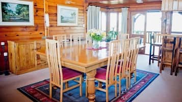A wooden dining area with a large table and chairs, framed artwork on the walls, and a view through the windows.