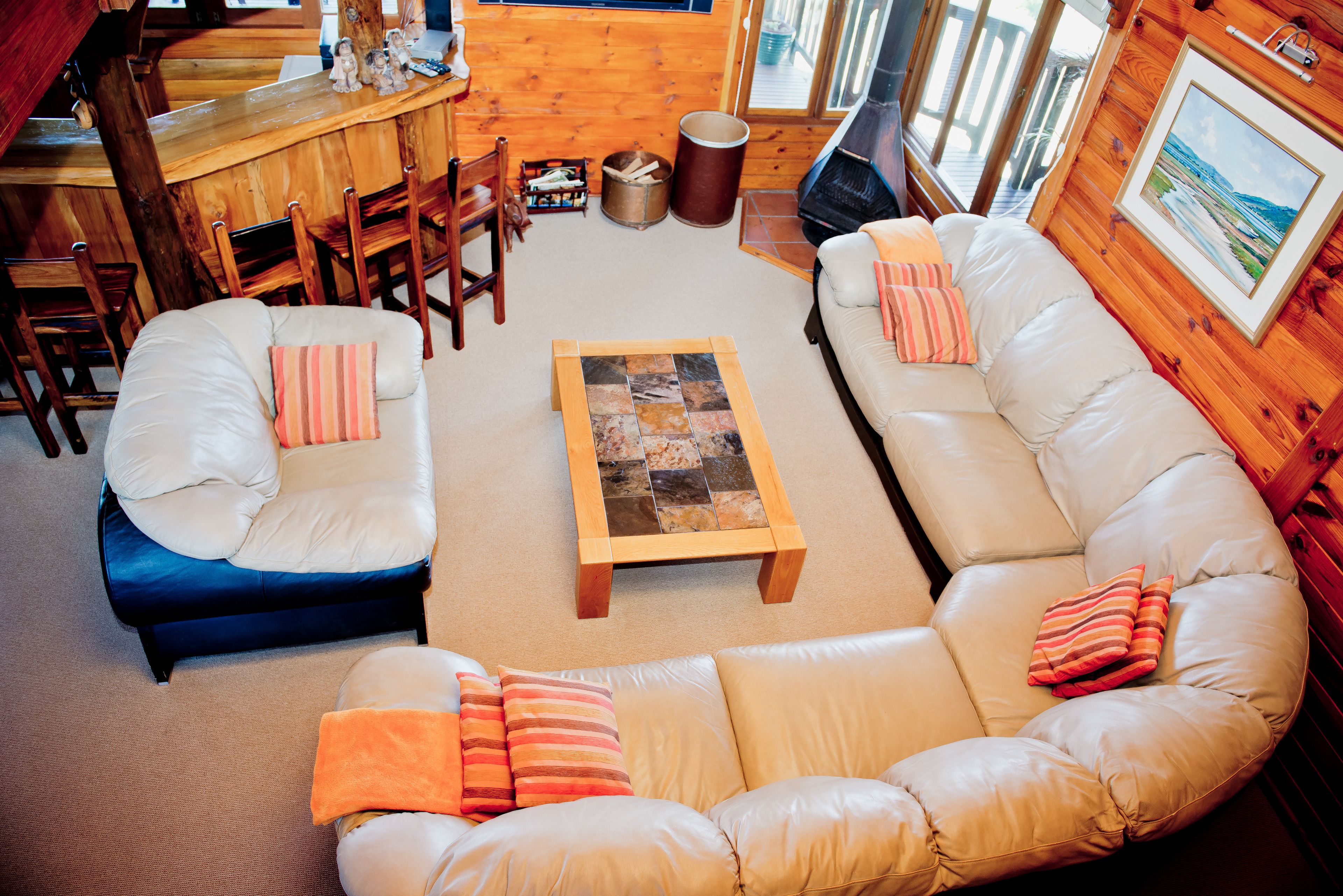 A cozy living room with a large beige sofa, a smaller blue sofa, and a wooden coffee table. There are two wooden chairs and a small table with decorative items.
