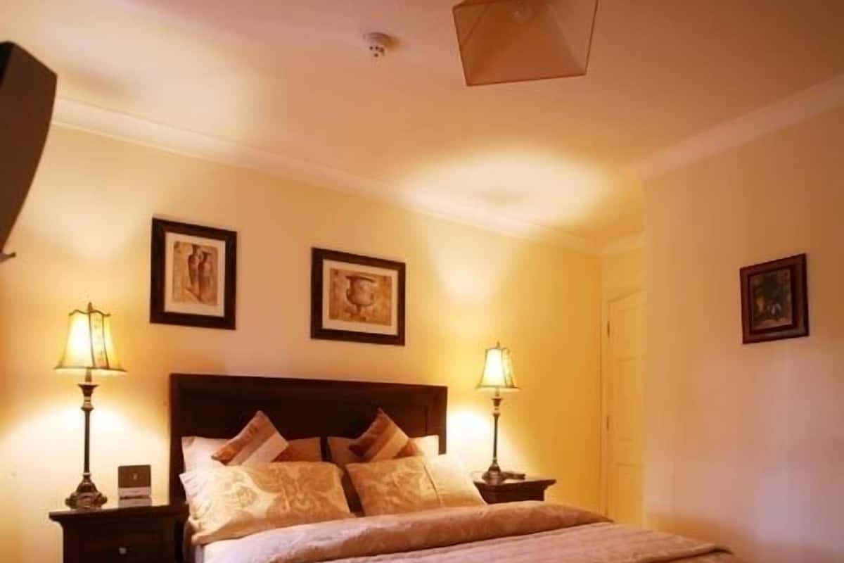 Un dormitorio con una cama grande, dos mesitas de noche con lámparas y cuadros enmarcados en la pared.