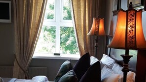 Une chambre à coucher avec un lit, des oreillers, une lampe et une fenêtre avec des rideaux.