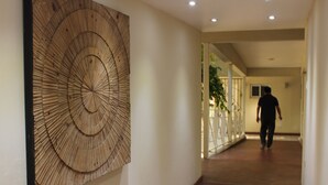 Un couloir avec une grande œuvre d’art en bois accrochée au mur, une personne qui marche et un escalier en arrière-plan.
