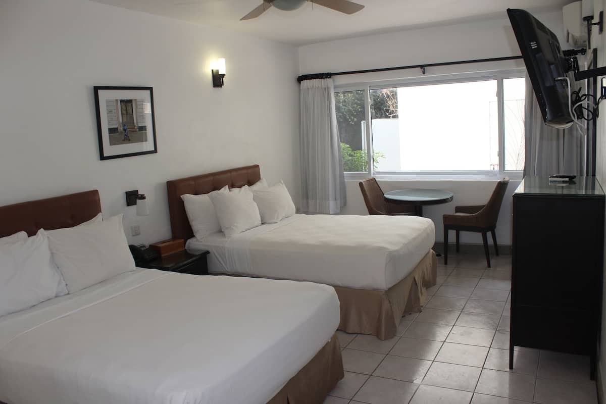 A hotel room with two beds, a desk, a chair, a TV, and a window with curtains.
