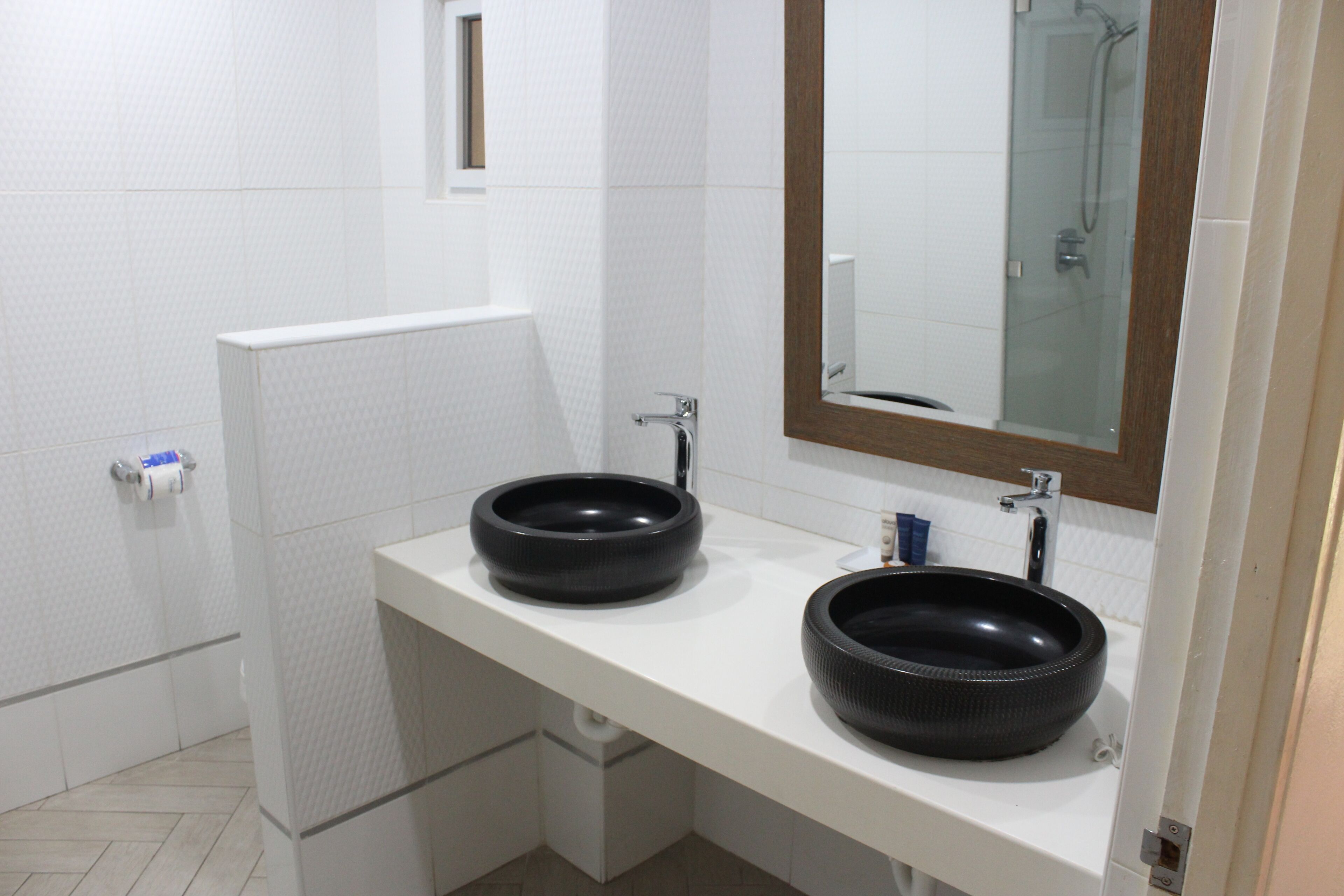 A modern bathroom with two black sinks, a white countertop, and a mirror with a wooden frame.