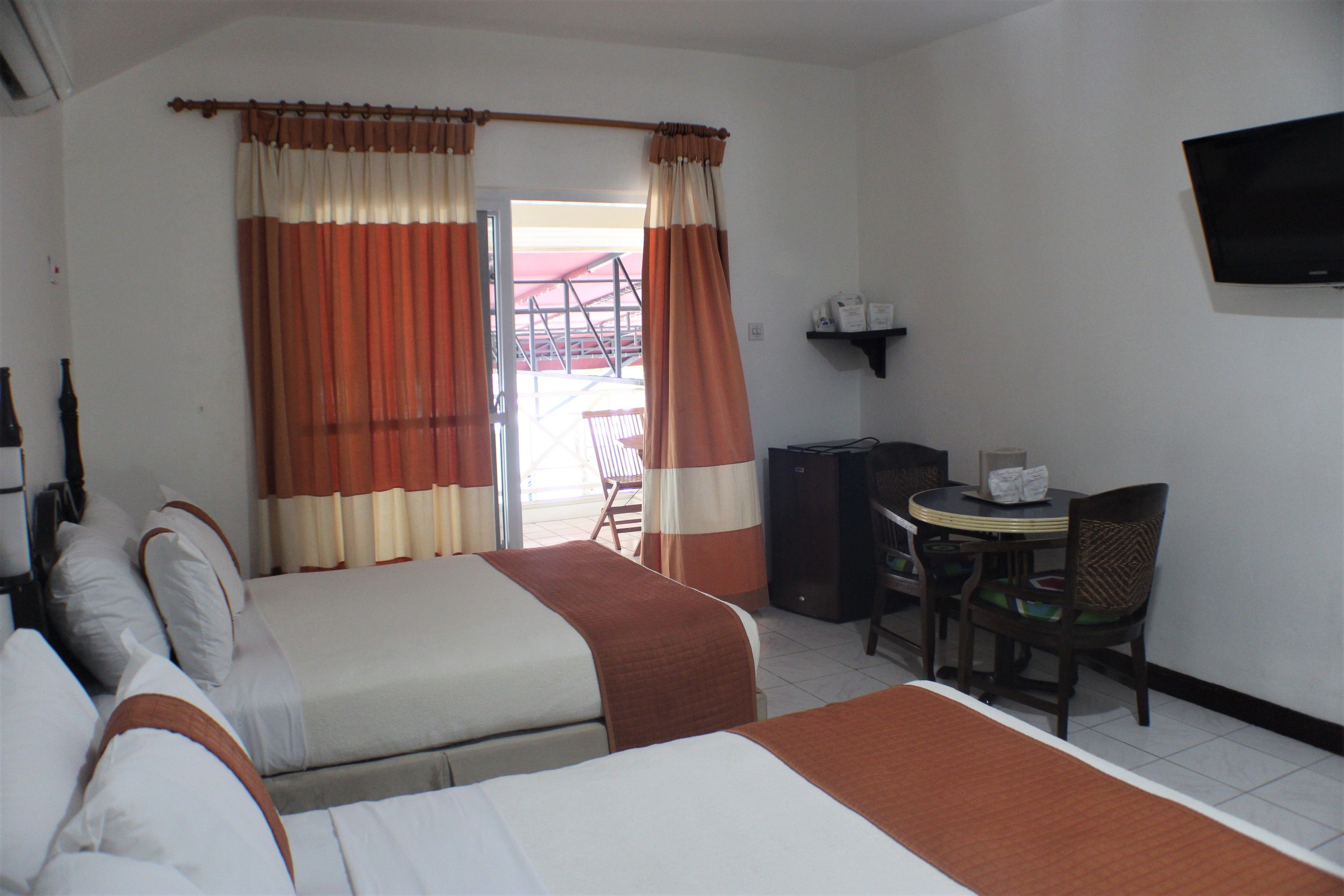 A hotel room with two beds, a desk with a chair, a television, and a window with curtains.
