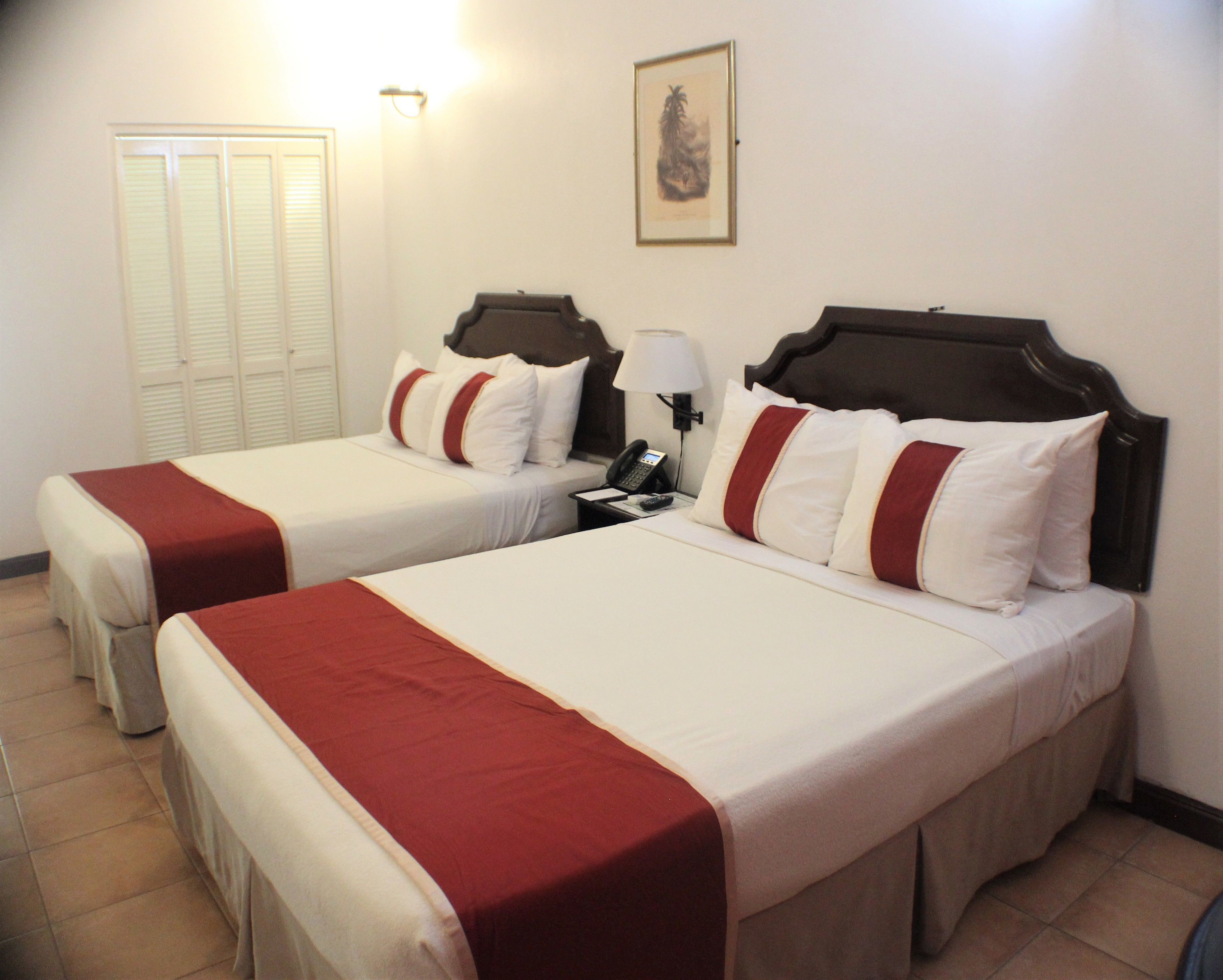 Une chambre d’hôtel avec deux lits, chacun agrémenté de draps blancs et de touches de couleur rouge, une table de chevet avec une lampe et un tableau encadré au mur.