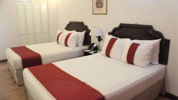 A hotel room with two beds, each with white bedding and red accents, a bedside table with a lamp, and a framed picture on the wall.