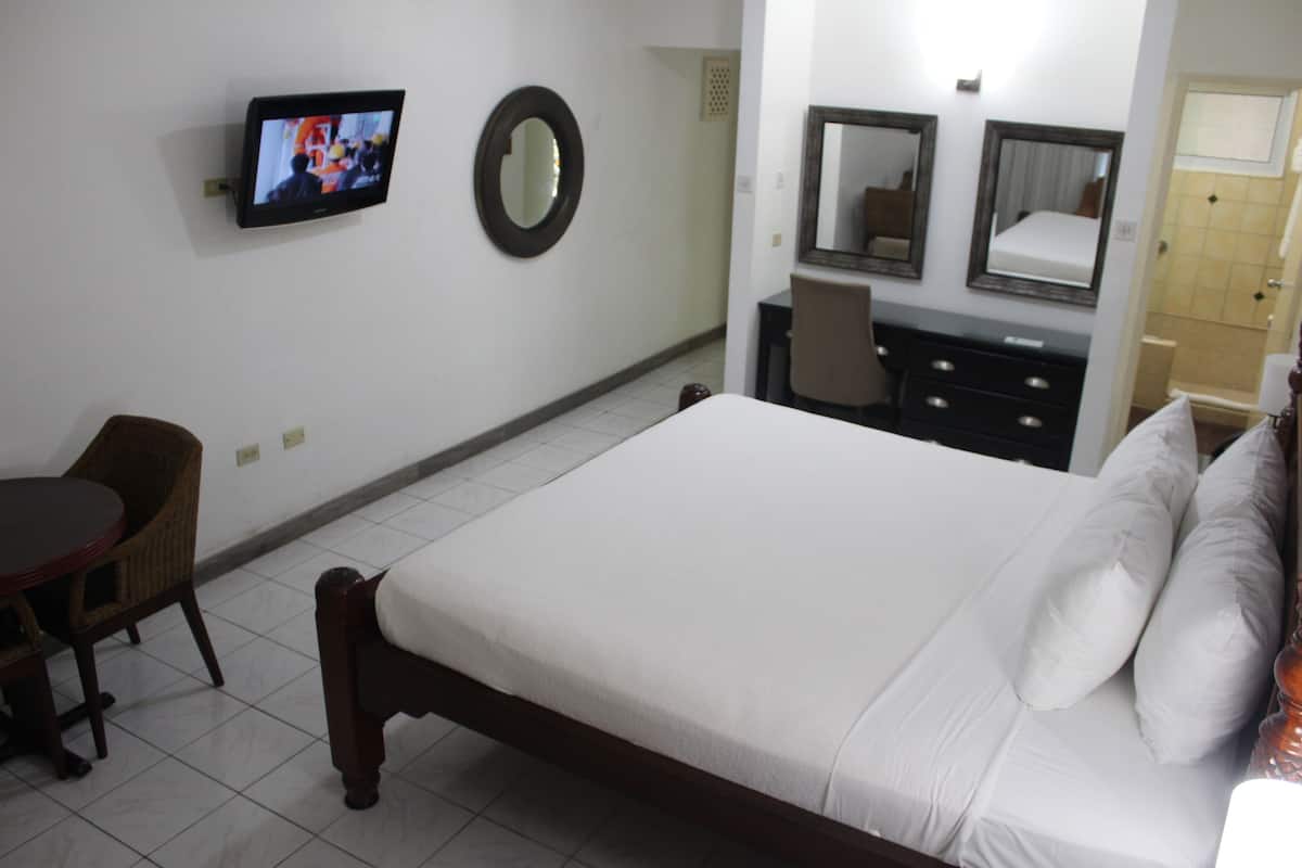 A hotel room with a bed, a TV mounted on the wall, a round mirror, a dresser, and a chair.