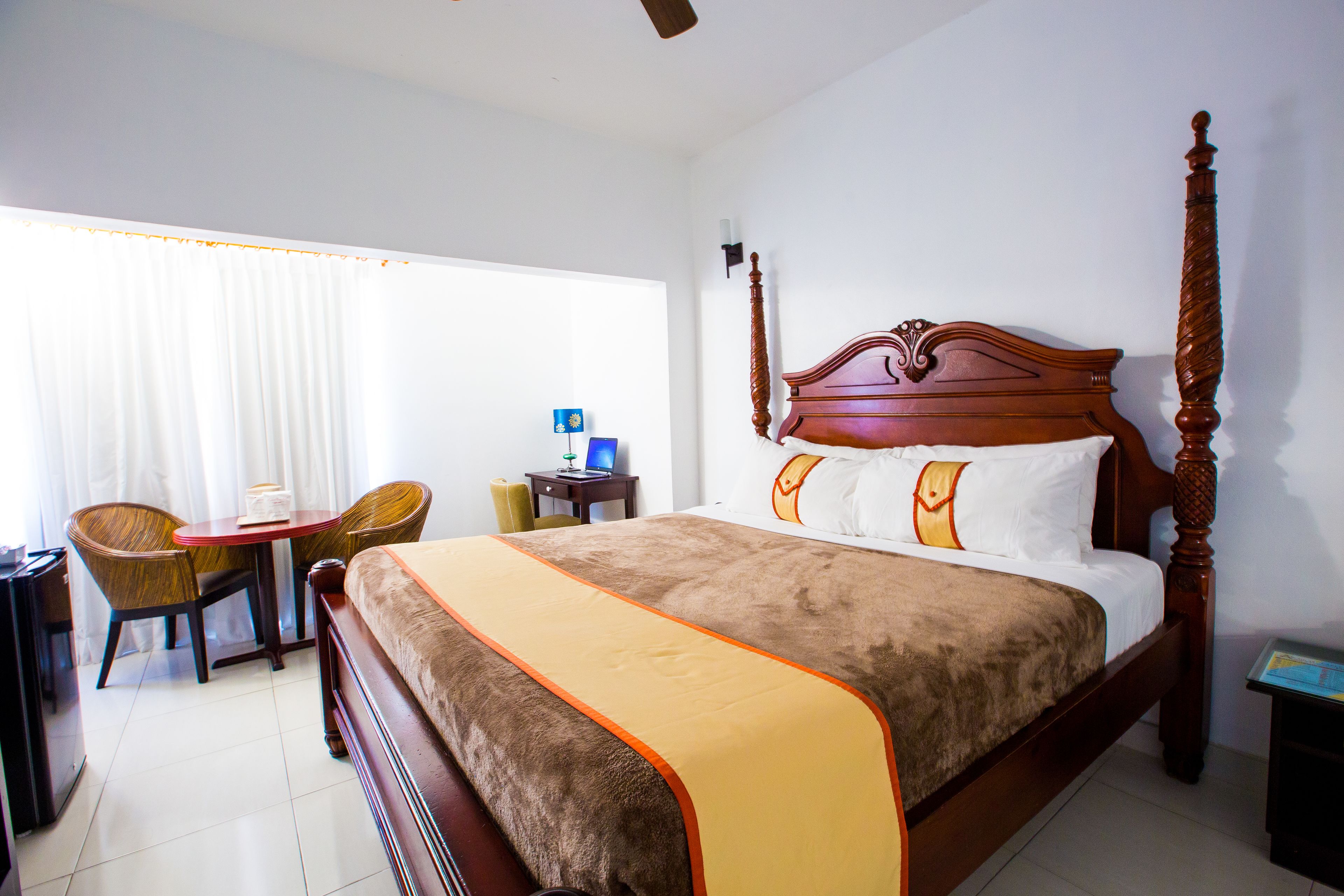 A hotel room with a four-poster bed, a desk with a chair, and a window with curtains.