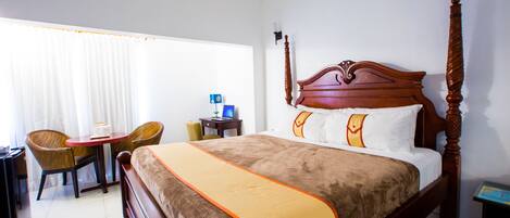 A hotel room with a four-poster bed, a desk with a chair, and a window with curtains.