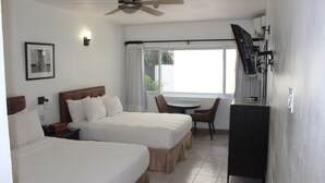 Une chambre d’hôtel avec deux lits, un bureau, une chaise, une télévision et un ventilateur de plafond.