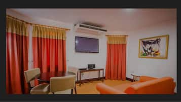A room with a dining table, two chairs, a sofa, a television, and a painting on the wall.