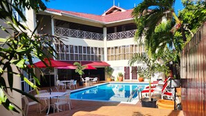 Un espace piscine avec une eau d’un bleu limpide, entouré de chaises et de tables blanches, et un parasol rouge offrant de l’ombre.