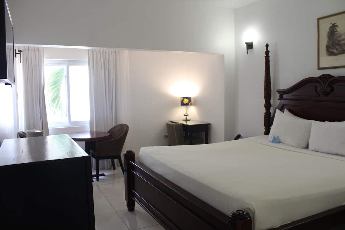 A hotel room with a large bed, a desk, a chair, and a lamp.