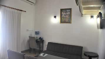 A room with a sofa, a dining table, a chair, a small table with a lamp, and a painting on the wall.