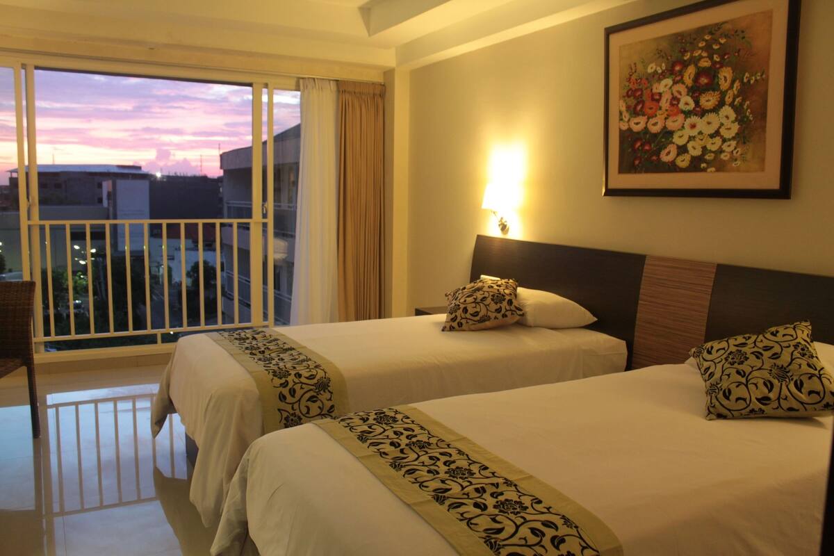 A hotel room with two beds, a balcony, a painting, and a view of the cityscape.