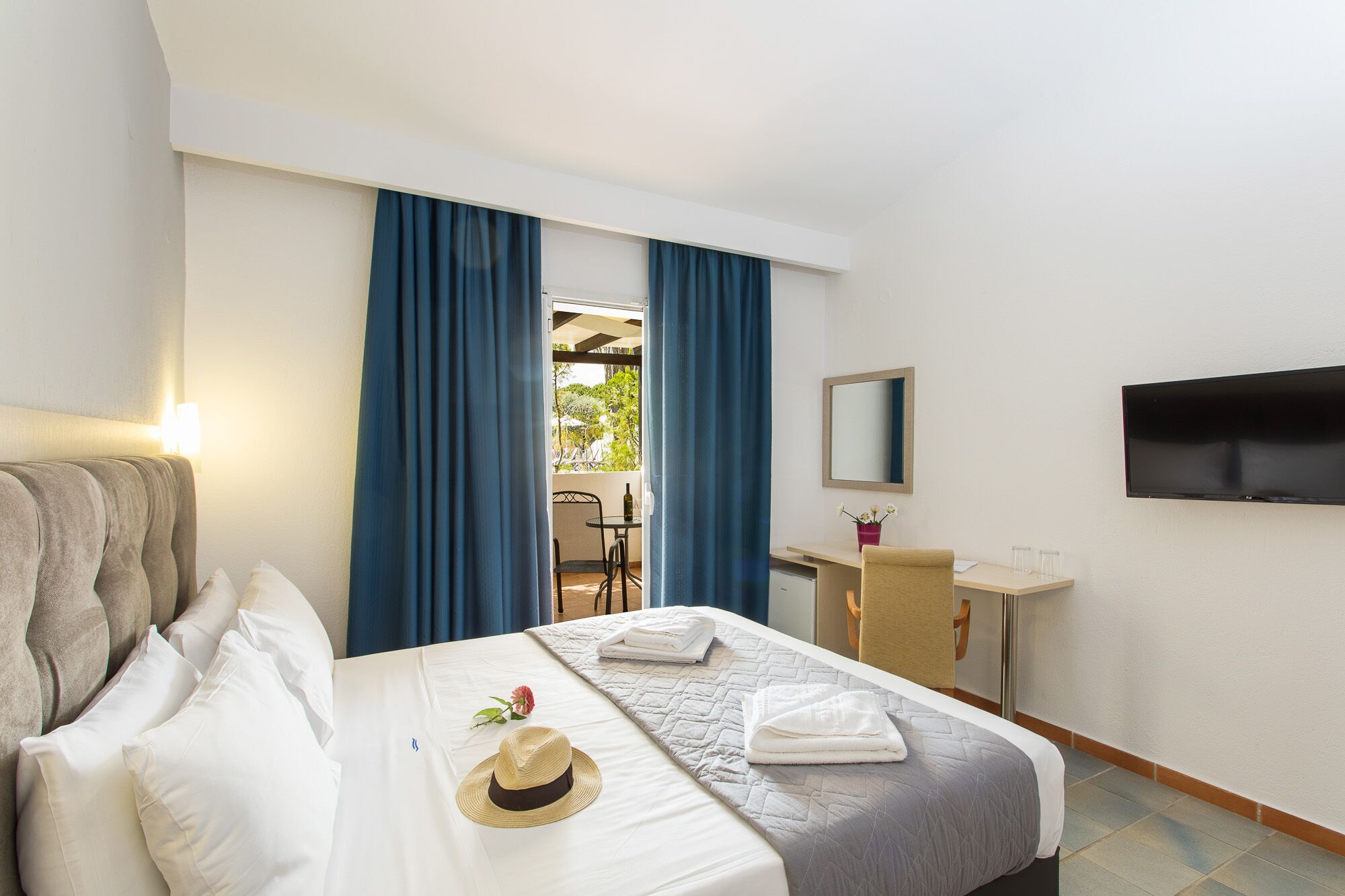 A hotel room with a bed, a desk, a TV, and a view of the outdoors.